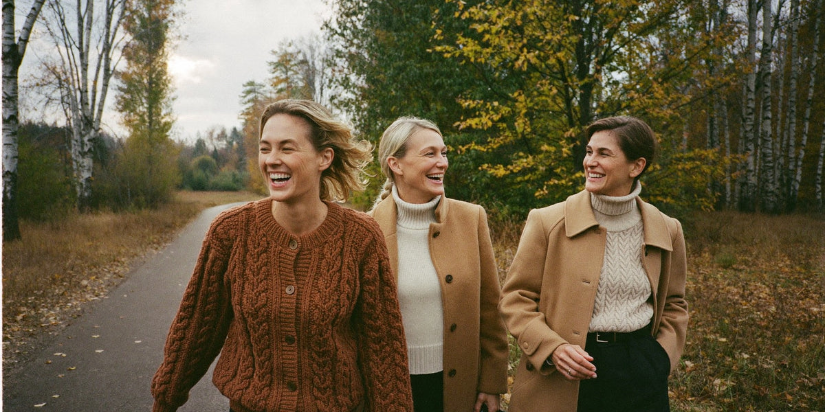 Four women in autumn knitwear standing in a birch meadow at golden hour